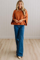BLONDE WOMAN WEARING DARK JEANS IN A BRIGHTLY LIT STUDIO WITH A SOLID SWEATER FEATURING SCALLOP TRIM AND BUTTONS UP THE SLEEVE IN THE COLOR HEATHERED RUST.
