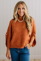 BLONDE WOMAN WEARING DARK JEANS IN A BRIGHTLY LIT STUDIO WITH A SOLID SWEATER FEATURING SCALLOP TRIM AND BUTTONS UP THE SLEEVE IN THE COLOR HEATHERED RUST.
