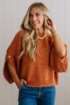 BLONDE WOMAN WEARING DARK JEANS IN A BRIGHTLY LIT STUDIO WITH A SOLID SWEATER FEATURING SCALLOP TRIM AND BUTTONS UP THE SLEEVE IN THE COLOR HEATHERED RUST.