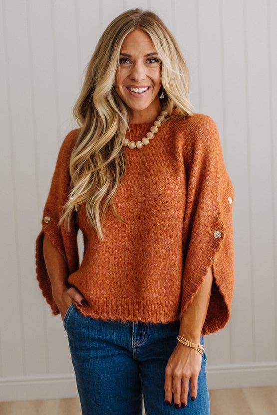BLONDE WOMAN WEARING DARK JEANS IN A BRIGHTLY LIT STUDIO WITH A SOLID SWEATER FEATURING SCALLOP TRIM AND BUTTONS UP THE SLEEVE IN THE COLOR HEATHERED RUST.