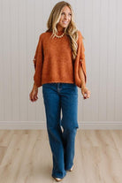 BLONDE WOMAN WEARING DARK JEANS IN A BRIGHTLY LIT STUDIO WITH A SOLID SWEATER FEATURING SCALLOP TRIM AND BUTTONS UP THE SLEEVE IN THE COLOR HEATHERED RUST.