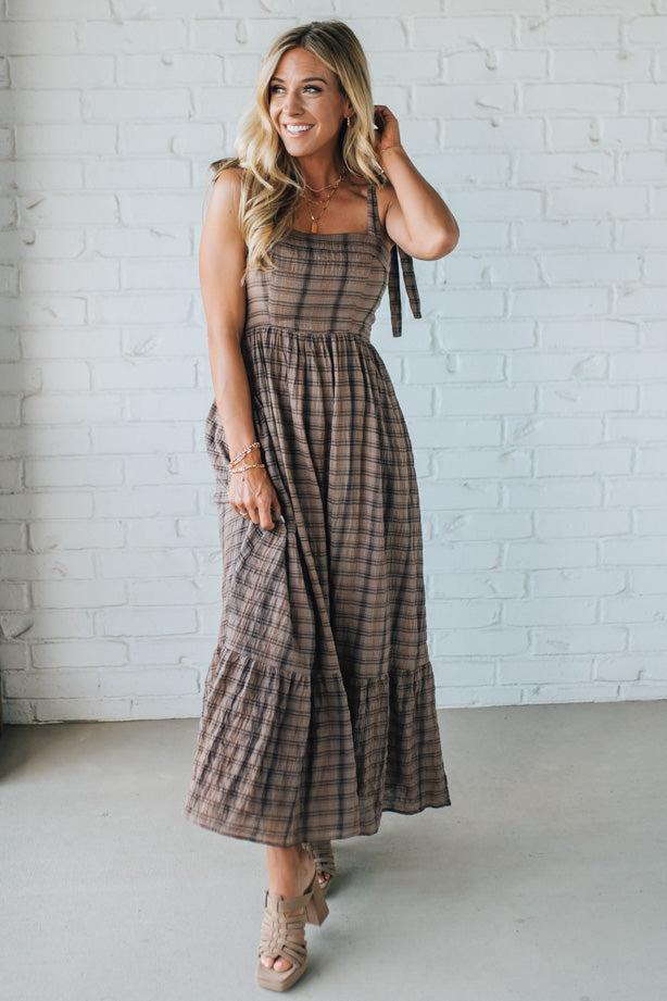 Woman wearing a plaid dress against a white brick wall.