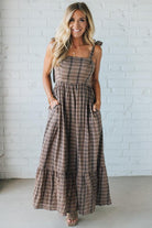 Woman wearing a plaid dress against a white brick wall.