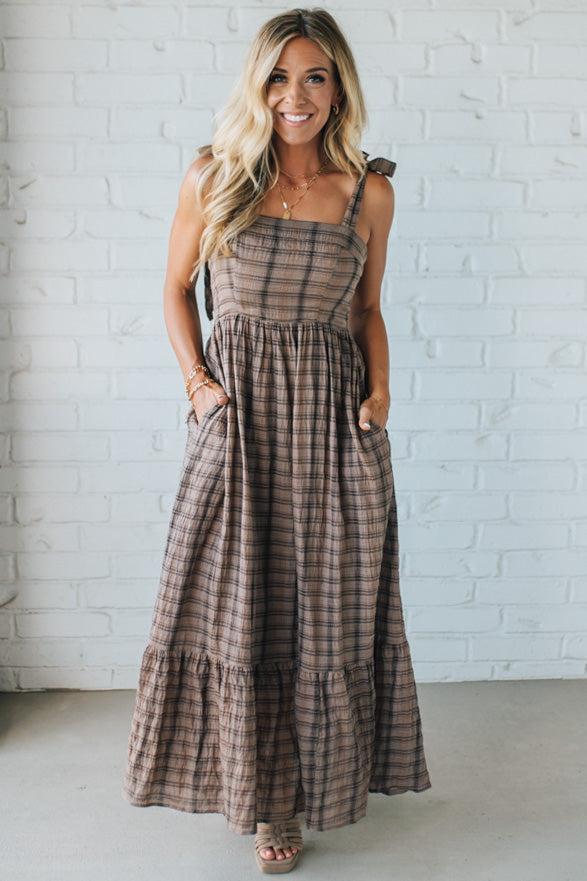 Woman wearing a plaid dress against a white brick wall.