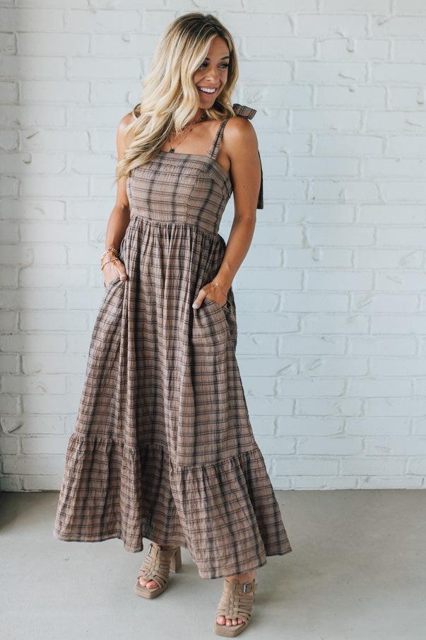 Woman wearing a plaid dress standing against a white brick wall.