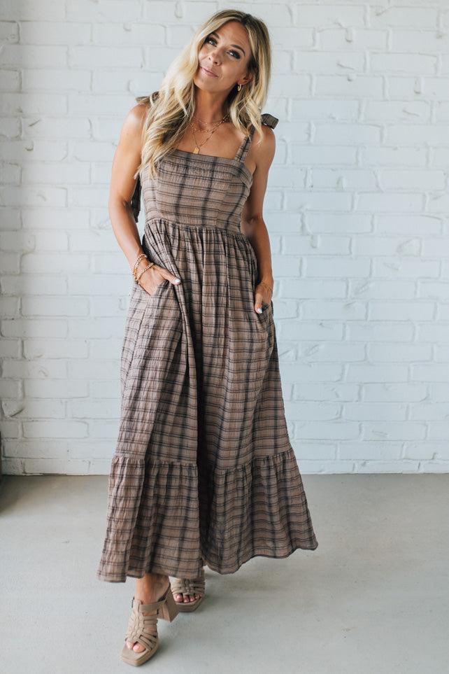 Woman wearing a plaid dress standing against a white brick wall.