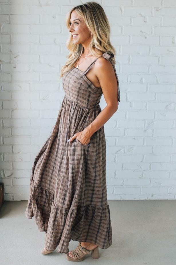 Woman wearing a plaid dress standing against a white brick wall.