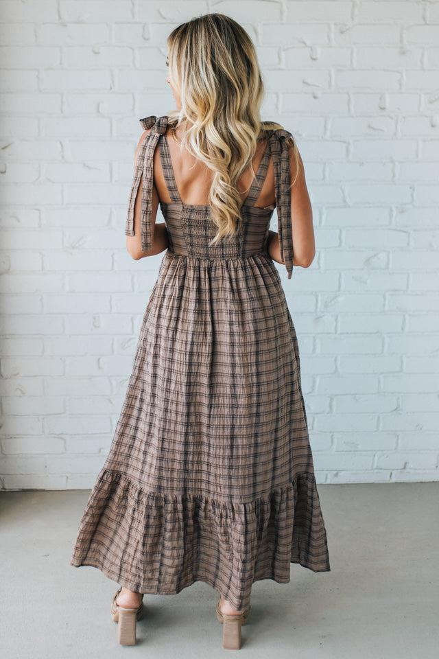 Woman wearing a plaid dress with a white brick wall background