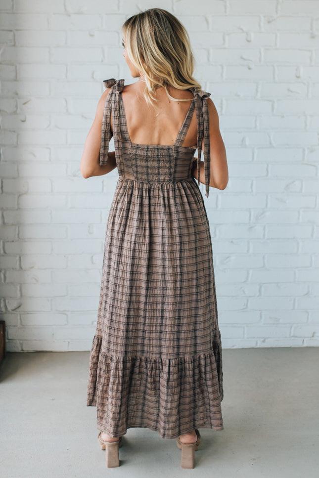 Woman wearing a plaid dress with a white brick wall background