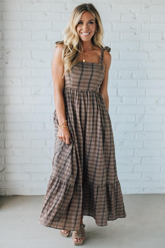 Woman wearing a plaid dress standing against a white brick wall.