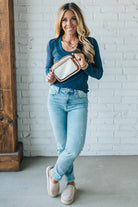 Woman holding a two tone belt bag against a white brick wall