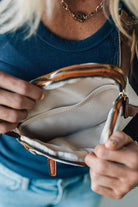 Person opening a white handbag with a gold zipper.