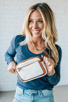 Woman holding a white handbag with brown trim against a plain background