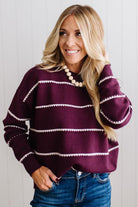 BLONDE WOMAN WEARING DARK JEANS IN A BRIGHTLY LIT STUDIO MODELING A CREW NECK, LONG SLEEVE, BLANKET STITCH STRIPED SWEATER IN DARK PLUM.