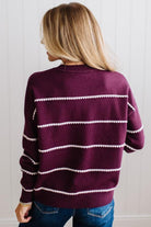 BLONDE WOMAN WEARING DARK JEANS IN A BRIGHTLY LIT STUDIO MODELING A CREW NECK, LONG SLEEVE, BLANKET STITCH STRIPED SWEATER IN DARK PLUM.