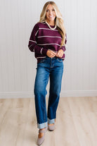 BLONDE WOMAN WEARING DARK JEANS IN A BRIGHTLY LIT STUDIO MODELING A CREW NECK, LONG SLEEVE, BLANKET STITCH STRIPED SWEATER IN DARK PLUM.