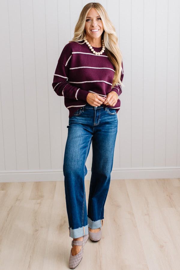 BLONDE WOMAN WEARING DARK JEANS IN A BRIGHTLY LIT STUDIO MODELING A CREW NECK, LONG SLEEVE, BLANKET STITCH STRIPED SWEATER IN DARK PLUM.