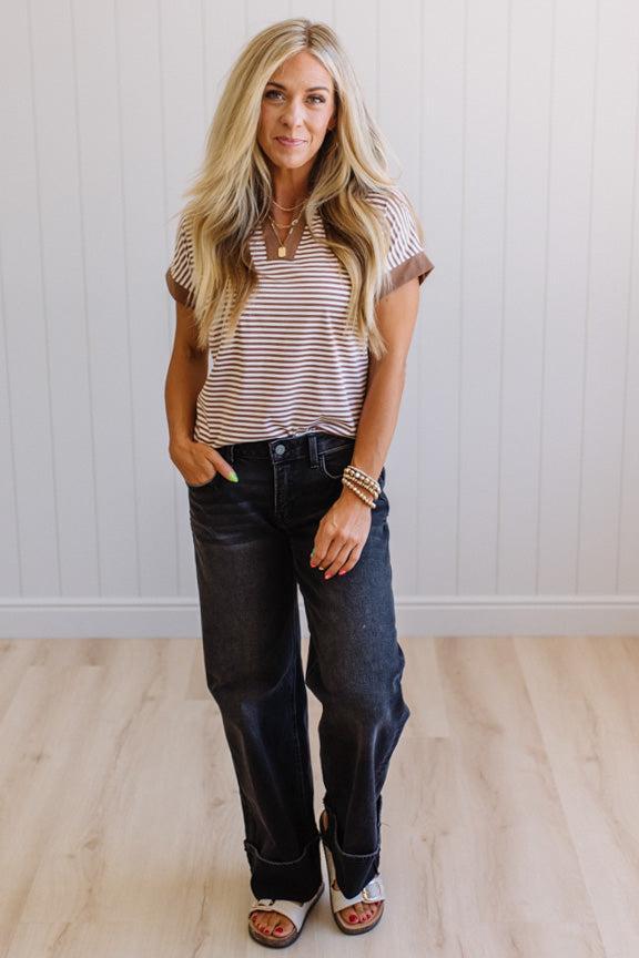 Woman wearing a striped shirt and jeans standing against a white wall.