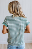 Woman wearing a green striped shirt and light jeans standing in a room with light wood flooring and white walls.