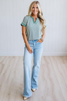 Woman wearing a green striped shirt and light jeans standing in a room with light wood flooring and white walls.