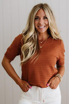 Woman wearing a rust-colored sweater and white pants against a light background