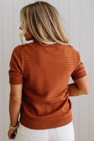 Person wearing a rust-colored sweater against a light wooden panel background