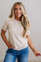 Woman wearing a beige sweater and blue jeans with a neutral background