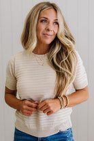 Woman wearing a beige knit sweater and blue jeans against a plain background