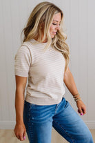 Woman wearing a beige knit sweater and blue jeans against a plain background
