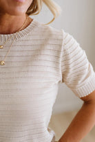 Woman wearing a beige knit sweater and blue jeans against a plain background