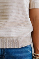 Close-up of a person wearing a beige knit top and blue jeans.