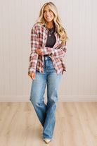 A woman modeling a red and white plaid button-down shirt over a dark top and blue jeans, standing in a room with light wood floors and white paneled walls.