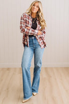 A woman modeling a red and white plaid button-down shirt over a black top, paired with light-wash blue flare jeans and beige pointed-toe flats, standing in a room with light wood floors and white paneled walls.