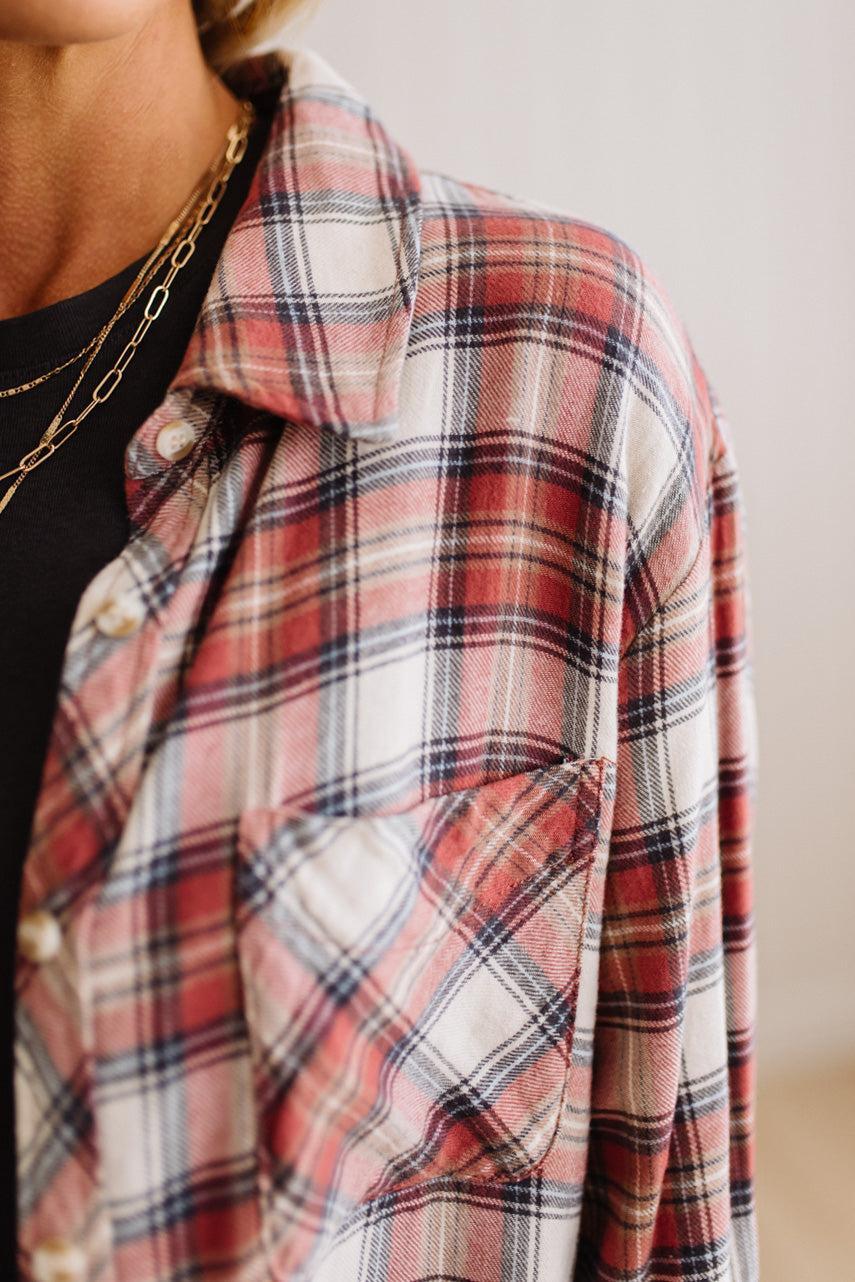 A close-up of a person wearing an oversized red, white, and navy plaid flannel button-up shirt over a black top, accessorized with layered gold chain necklaces.