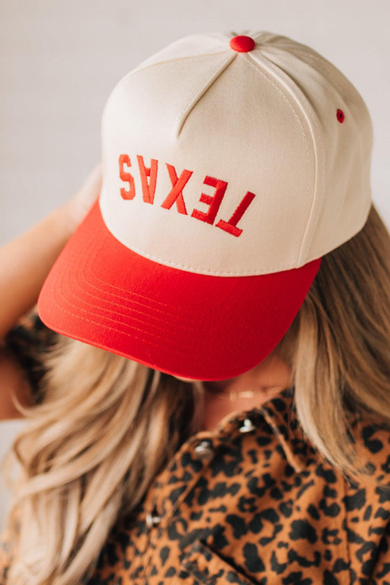 Blonde woman in leopard dress wearing a cream hat with red brim and red TEXAS embroidered upside down at the front.