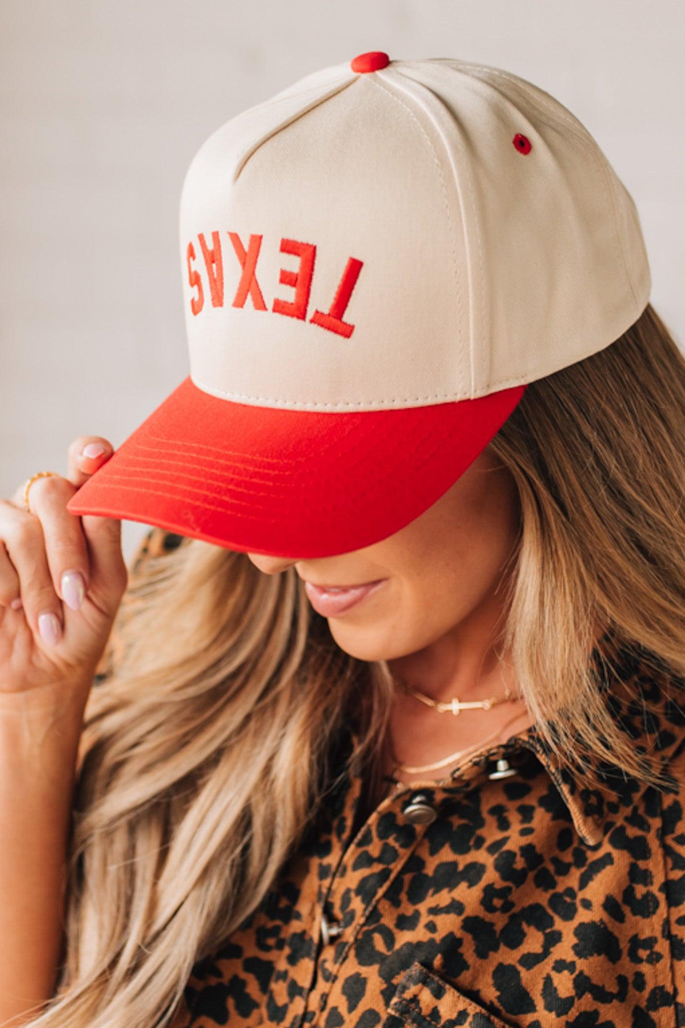 Blonde woman in leopard dress wearing a cream hat with red brim and red TEXAS embroidered upside down at the front.