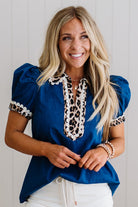 Woman wearing a blue blouse with leopard print details against a white background