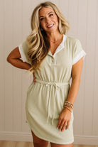 Woman wearing a light green dress with white accents against a beige wall.