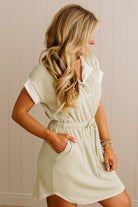 Woman wearing a light green dress with a white collar against a beige wall.