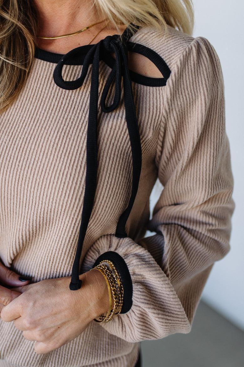Beige ribbed sweater with black ribbons and a plain background