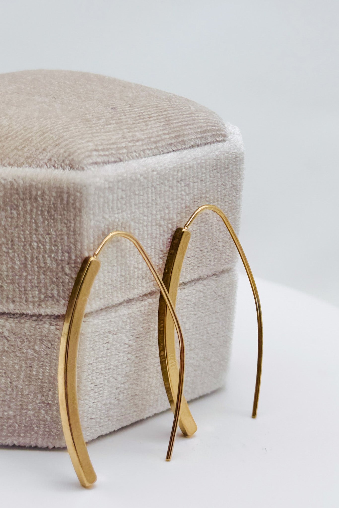 Gold hoop earrings on a textured beige cushion with a light gray background