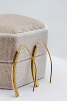 Gold hoop earrings on a textured beige cushion with a light gray background