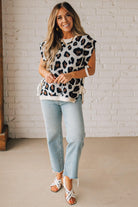 Blonde woman wearing a cream short sleeve sweater with all over bold brown and black leopard pattern, and double white ties on each side.