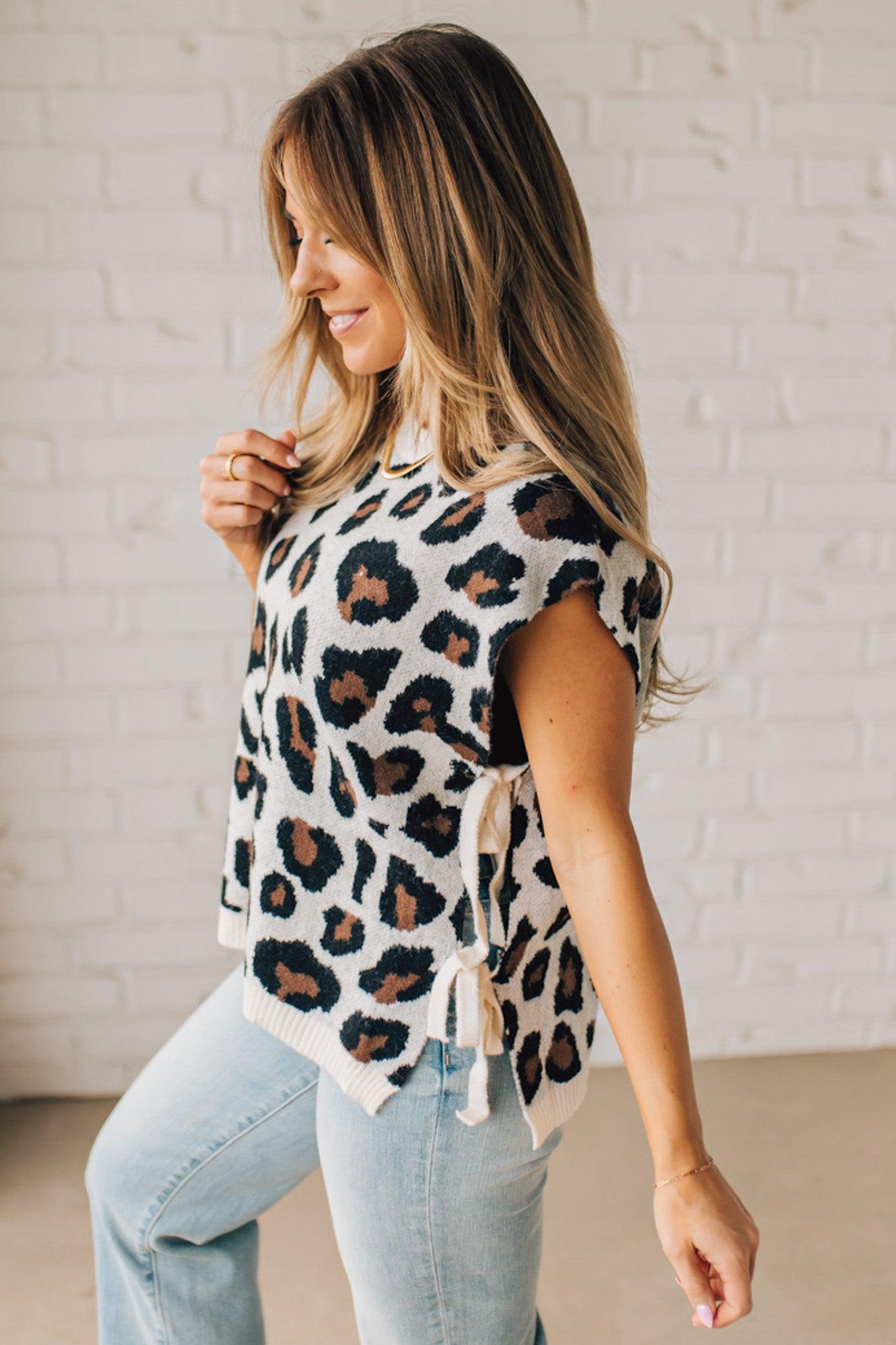 Blonde woman wearing a cream short sleeve sweater with all over bold brown and black leopard pattern, and double white ties on each side.