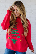 Woman wearing a red Christmas sweater with decorative text and stars against a white brick wall.