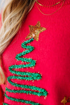 Red sweater with green embroidered tree and gold star design.