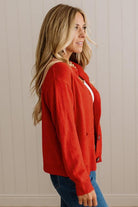 Blonde woman in dark jeans and a bold red-orange cardigan with black button toggles down with front and side pockets.
