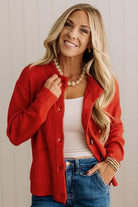 Blonde woman in dark jeans and a bold red-orange cardigan with black button toggles down with front and side pockets.