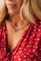 Close-up of a person wearing a red patterned top and a necklace with a circular pendant.