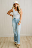 Woman wearing a light gray tank top, blue jeans, and a white cap indoors.